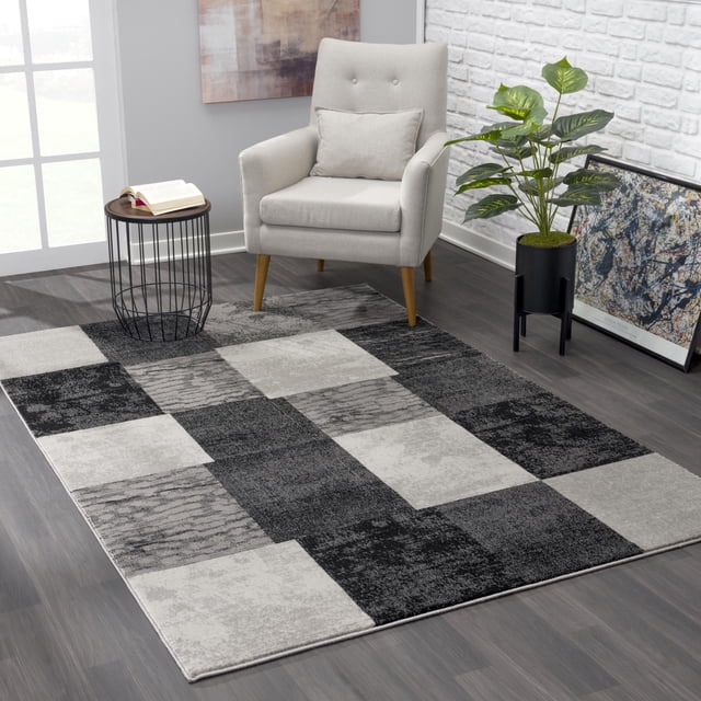 Rug Branch Montage Collection Tapis Coureur Moderne Géométrique en Gris Présentant un Motif Tissé à Haute Densité de Carrés Texturés Clairs et Foncés, Posé sur un Plancher Stratifié Foncé dans une Pièce Moderne avec un Fauteuil Gris Pâle, une table d'Appoint en Fil Noir avec un Livre Ouvert, une Plante en Pot Verte et une Oeuvre Murale Abstraite. Idéal pour Salons, Couloirs Ou Entrées.