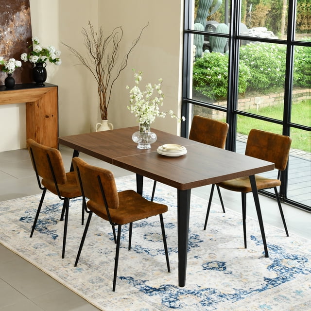 Homy Casa 5 Pieces Modern Dining Set with Faux Suede Chairs and Faux Walnut Table featuring a rectangular faux walnut tabletop with black flat iron legs, four brown faux suede chairs with ergonomic backrests and footrests, arranged on a blue and white patterned rug in a bright dining room with large black-framed windows overlooking a garden, ideal for home or commercial dining spaces.