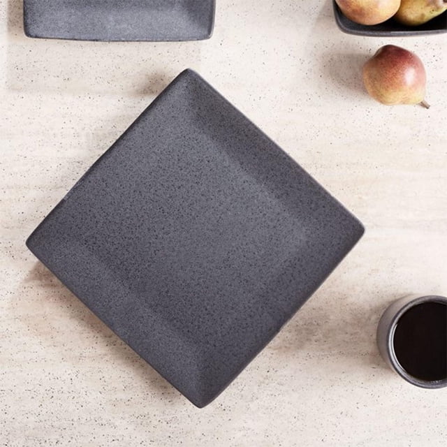 Better Homes & Gardens Anderson Dark Grey Square-Shaped Dinner plate made of durable ceramic stoneware with a mottled reactive glaze finish, shown top-down on a light speckled surface with pears and a coffee cup, suitable for everyday dining and microwave use.