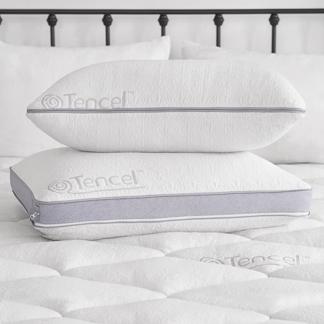 Sleep Innovations Customizable Comfort Gel Memory Foam Pillow in standard size, featuring adjustable firmness and cooling support. The white pillow with a soft, breathable Tencel cover and grey accents is shown stacked on a quilted mattress. Designed to maintain shape and comfort, it comes with a 5-year warranty.