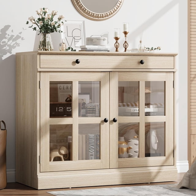 35.4" sideboard buffet cabinet with glass doors and oak finish, featuring a spacious drawer and adjustable shelves for versatile kitchen storage. The sturdy walnut construction and soft-close doors ensure durability and quiet functionality. Glass doors elegantly showcase dinnerware and decor, making it ideal for dining rooms, kitchens, or as a buffet table, coffee bar, or TV stand. Positioned in a bright, modern room with decorative accents on top.