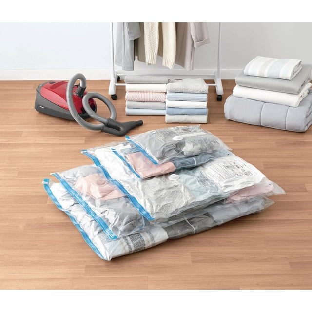 Mainstays Ensemble de Sacs de Rangement sous Vide Polyvalents avec Cinq Sacs Transparents Scellés sous Vide Contenant des Vêtements et du Linge Pliés sur un Plancher en Bois à Côté d'Un Aspirateur Rouge, avec des Couvertures Pliées et des Vêtements sur une Étagère Blanche en Arrière-Plan, Convient à l'Organisation des Vêtements et du Placard et aux solutions de Rangement Gain de Place.