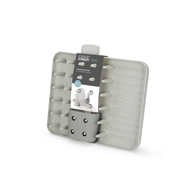 Joseph Joseph Égouttoir à Vaisselle Compact DUO en Gris Pâle avec Dents Largement Espacées pour Sécher la Vaisselle, un pot à Ustensiles Mobile, base Nervurée Inclinée pour Canaliser l'Eau, et Bec Intégré pour l'Égouttage dans l'Évier, Montré Incliné sur un Fond Blanc. Sa Conception Compacte Est Également Idéale pour Organiser de Petits Outils de Cuisine.