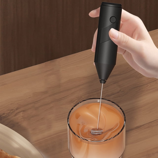 LSLJS Electric Milk Frother Maker Mini Coffee Maker Whisk Hand Coffee Frother Cappuccino Creamer in black, shown in use frothing milk in a glass. The handheld frother features a compact design with an oval-shaped whisk and requires 2 AA batteries (not included). Ideal for creating creamy foam for coffee, cappuccinos, and lattes, it is lightweight and portable, measuring 21x3.8 cm. Suitable for home, office, or restaurant use.