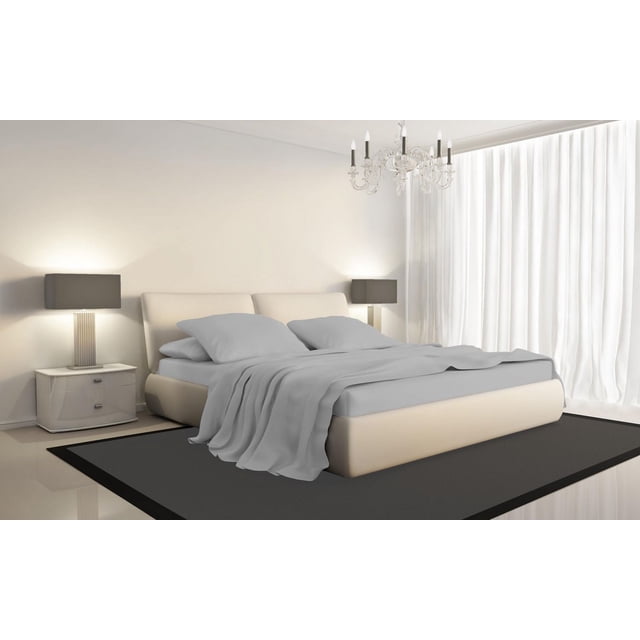 Johnson Home 600 Thread Count Organic Cotton Sheet Set on a beige upholstered bed with smooth light grey fitted sheet, flat sheet, pillowcases, and a loosely draped blanket in a minimalist bedroom with white walls, matching bedside tables with grey lamps, a dark rug, sheer white curtains, and a crystal chandelier.