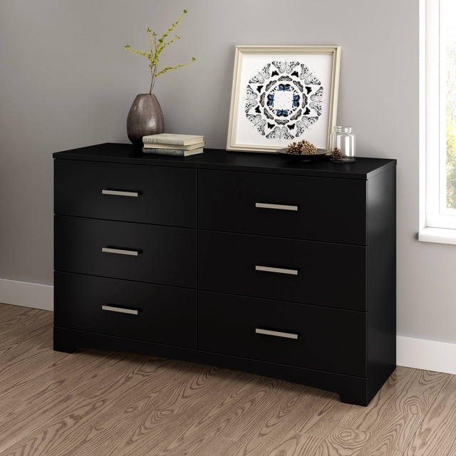 South Shore Gramercy 6-Drawer Dresser for Adult in pure black with six spacious drawers and straight metal handles, featuring a slightly curved kick plate, shown on wood flooring against a light wall, decorated with a vase, books, framed butterfly artwork, and pinecones, suitable for organized storage in kids' bedrooms.