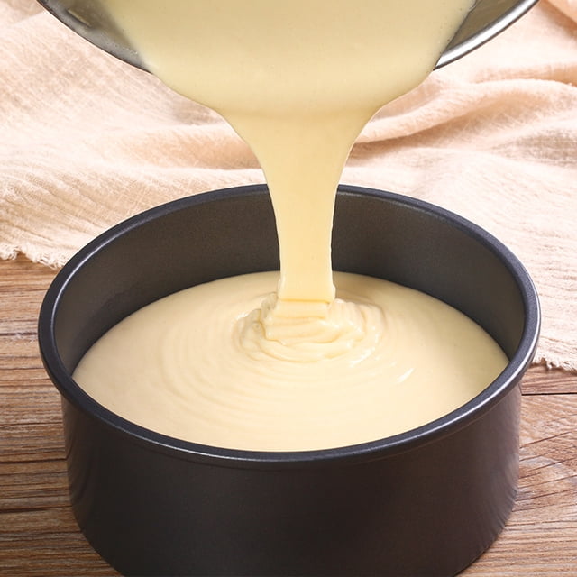 Dvkptbk Cake Moulds Factory Direct Cake Baking Pan made of durable metal with a non-stick coating, shown in use with batter being poured into the round pan. The pan measures 16x16x6.5cm (6.3x6.3x2.56in) and is designed for even heat distribution, making it ideal for baking cakes. The image is set on a wooden surface with a beige fabric in the background.