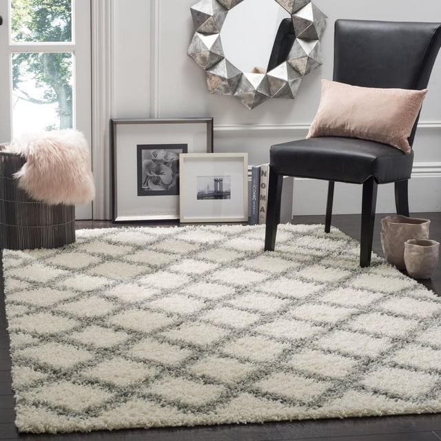 Safavieh Dallas Jerrie Tapis Shag Géométrique avec un Motif de Losanges Pelucheux dans des Tons Crème et Gris, Posé sur un Plancher de Bois Franc Foncé sous une Chaise en Cuir Noire avec un Coussin Rose, photos Noir et Blanc Encadrées Près et un Miroir à Facettes Géométriques, Idéal pour des Espaces Domestiques Durables et Très Passants.