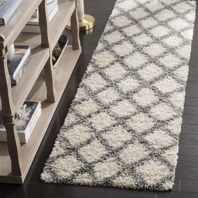 Safavieh Layla Geometric Plush Shag Area Rug runner with cream and grey diamond pattern, dense synthetic fiber pile on dark hardwood floor beside a beige wooden bookshelf, suitable for high traffic areas and often used as an accent rug in narrow spaces.