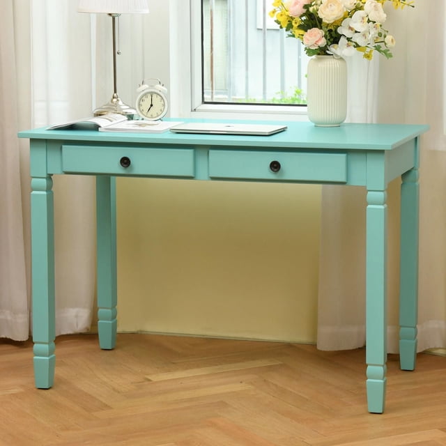 Homylin Home Office Desk with 2 Drawers, 43-inch green writing computer desk with a sleek modern design and turned legs, placed by a window with white curtains, styled with a silver lamp, white alarm clock, open book, closed laptop, and a white vase with mixed flowers, ideal for writing, studying, or as a makeup vanity.