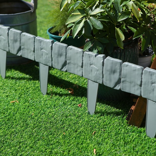 Vaidha 10PCS Plastic Border Edging Garden Grass Fence Wall in a gray finish, shown installed on a grassy lawn. The flexible plastic edging features a textured design resembling stone tiles and is connected in a straight line. Ideal for defining garden beds, flower beds, or lawn edges, the set includes 10 pieces, each measuring 25x23 cm, for a total length of 5 meters. The edging is easy to install by inserting into soft ground or trenching for harder surfaces.
