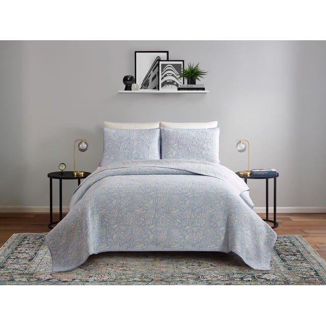 Light blue Better Homes & Gardens quilt featuring an intricate floral pattern, displayed on a neatly made bed with matching pillow shams in a contemporary bedroom.