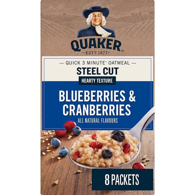 Quaker Boîte de Saveur d'Avoine à Cuisson Rapide, Coupe Acier, Bleuets et Canneberges sur une surface en Bois avec Flocons d'Avoine Éparpillés, Bleuets et Canneberges. l'Emballage Met en Valeur une Cuisson Rapide de 3 Minutes, texture Copieuse, Arômes Entièrement Naturels, et Contient 8 Sachets. une Cuillère de Gruau avec Bleuets et Canneberges Est Montrée à l'Avant.