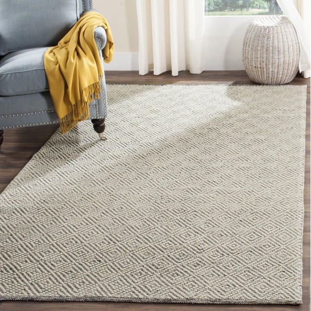 Safavieh Natura Eanna Geometric Area Rug, Ivory and Light Grey, 6' x 9', handwoven with soft, lustrous yarns forming a textured geometric mosaic pattern with oversized loops and flat weaves. Laid on hardwood floors beside a grey armchair draped with a mustard throw and a woven basket near a window with white curtains, suitable for casual and beach house decor.