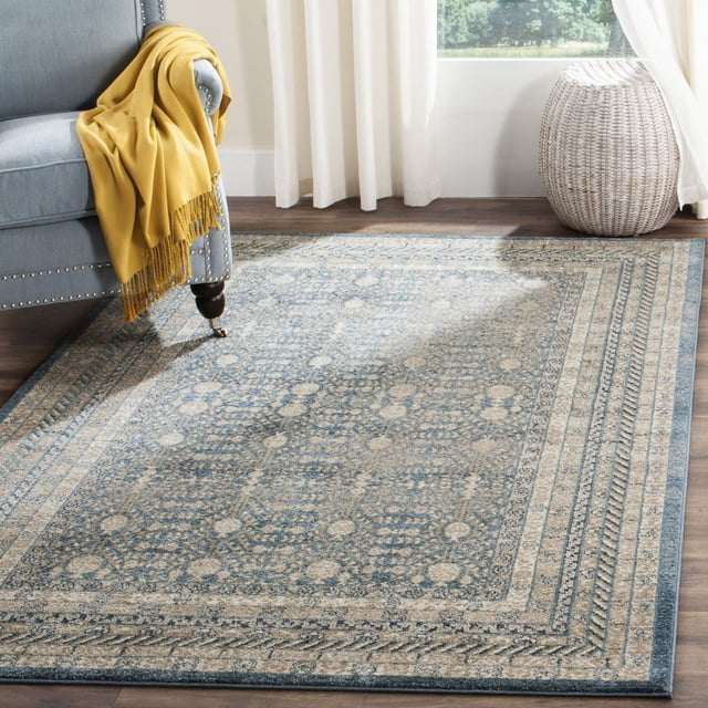 SAFAVIEH Sofia Cionadogh Border Area Rug featuring traditional motifs and distressed-look patina in muted blue and beige tones, placed on hardwood flooring beside a grey upholstered armchair with a mustard yellow throw, near white curtains and a woven basket by a window, suitable for adding classic style to living spaces.