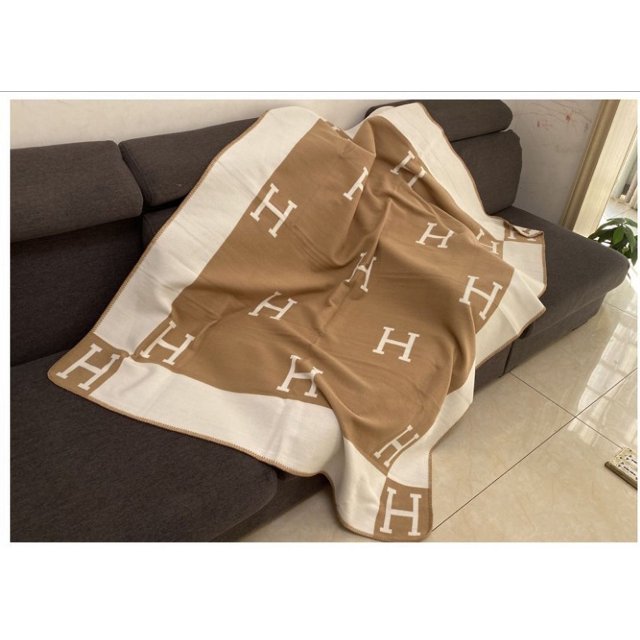 Couverture de Climatisation Couverture Couverture en Flanelle Couverture de Camping en Fibre de polyester, Mesurant 130 cm de Largeur et 160 cm de Longueur. la Couverture Présente un design beige et Blanc avec des Motifs « H » Répétés, Exposée Drapée sur un sofa Gris Foncé dans un Cadre de Salon Moderne. Convient à Toutes les Saisons et Pèse entre 1000 g et 1500 g.