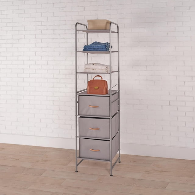 Mainstays Tour de Rangement à 7 Niveaux avec Tiroirs avec Cadre en Métal Gris Mat et Étagères en Tissu, Comprenant Quatre Étagères Ouvertes Tenant des Vêtements Pliés, un Sac à Main et une Boîte de Rangement, plus Trois Tiroirs en Tissu avec Poignées Beige, Posé sur un Plancher de Bois Clair contre un Mur de Briques Blanc, Conçu comme un Organisateur de Garde-Robe portable Idéal pour le Rangement de Vêtements et d'Accessoires.