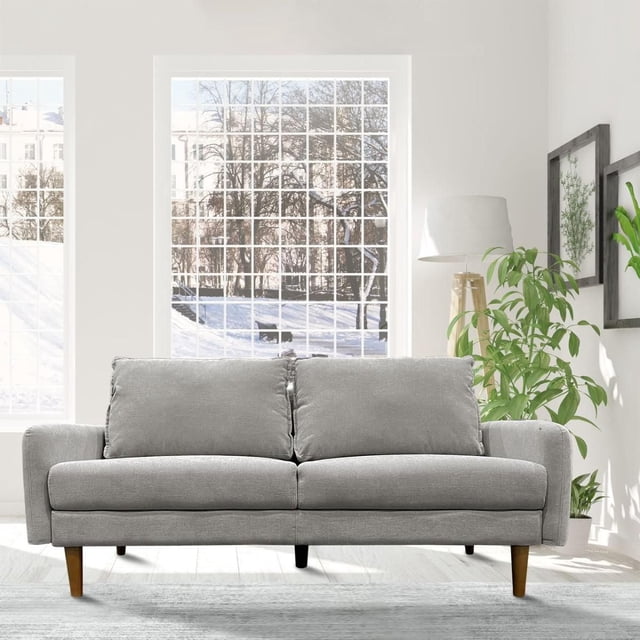 Oliver 3-Seater Sofa, Grey, front-facing in a bright living room with large windows showing a snowy landscape. This contemporary sofa has slim arms, splayed wooden legs, and a durable 100% polyester fabric cover. Positioned on light wood flooring with green plants and framed botanical art, it suits modern living room furniture and seating needs.