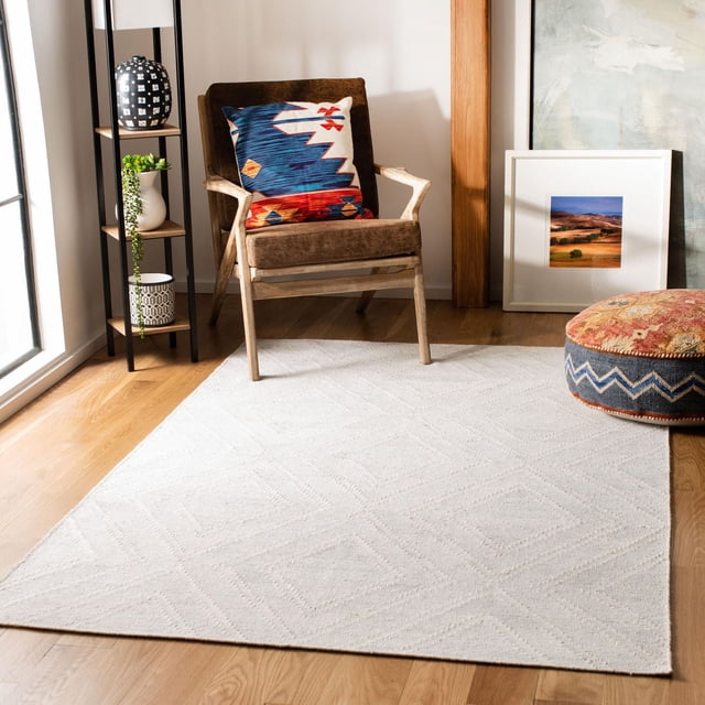 Safavieh Kilim Lorcan Tapis à Losanges Géométriques Présentant une texture de Laine Tissée Plate Indigène avec de Subtils Motifs de Losanges dans une Teinte Légère Neutre, Posé sur un Plancher de Bois Franc dans une Pièce Lumineuse avec un Fauteuil en Bois Brun Tenant un Coussin Coloré d'Inspiration Tribale, une Étagère en Métal Noire avec des vases Décoratifs et un pouf à Motif Rond, Idéal pour un accent durable dans les Aires de Vie.