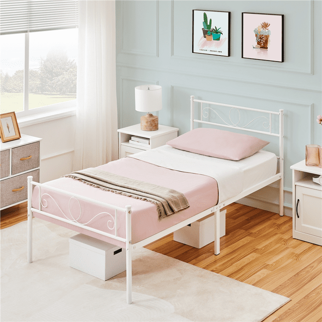 Yaheetech Lit Plateforme en Métal à Volutes Élégant pour Lit Simple avec Tête de Lit et Pied de Lit en Blanc, Exposé dans une Chambre à Thème Pastel. le Cadre de Lit Est Fabriqué en Métal durable avec un Volutes Complexe sur la Tête de Lit et le Pied de Lit. Il Présente Plusieurs Pieds de Soutien pour la Stabilité et un design à Lattes Qui Prend en Charge Tous les types de Matelas Sans Sommier. le Cadre Offre 12,6 Pouces de Liquidation sous le Lit pour un Rangement Pratique. la Chambre Comprend une Literie Rose Douce et une Déco Complémentaire.