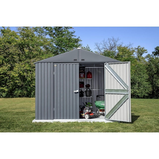 Arrow Elite Steel Storage Shed, 10x8, Anthracite, front view with one door open showing organized garden tools including lawn mower, fertilizer spreader, watering can, and shelving with outdoor supplies on a grassy lawn with trees behind, suitable for outdoor storage and garden equipment.