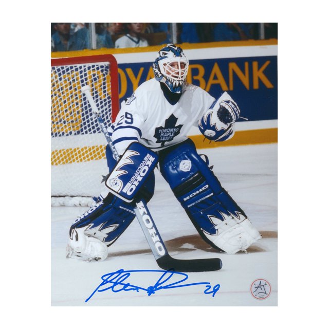 Felix Potvin Autographed Toronto Hockey Home Ice 8x10 Photo featuring Felix Potvin in a white Toronto Maple Leafs uniform during gameplay on home ice. The photo is professionally printed on high-quality photo paper and includes a hand-signed autograph in blue ink. Certified authentic by AJ Sports with a hologram and certificate of authenticity.