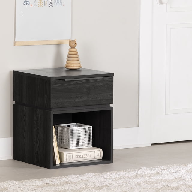 South Shore Hourra 1-Drawer Nightstand for Child in dark wood finish, with a single drawer featuring a slim metal handle and an open lower shelf holding books and a small basket, positioned against a light wall near a white door with a wooden toy on top.