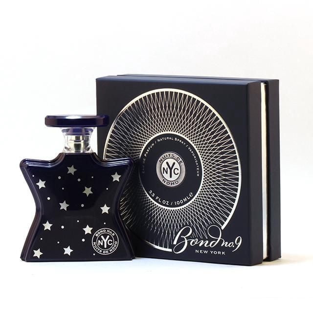 Bond No 9 Nuits De Noho Eau De Parfum Spray For Women 100ml showing a star-shaped dark blue glass bottle with silver stars and a flat round cap, next to a black box with a silver circular geometric design and Bond No 9 New York branding, a fruity-floral gourmand fragrance suitable for evening wear.