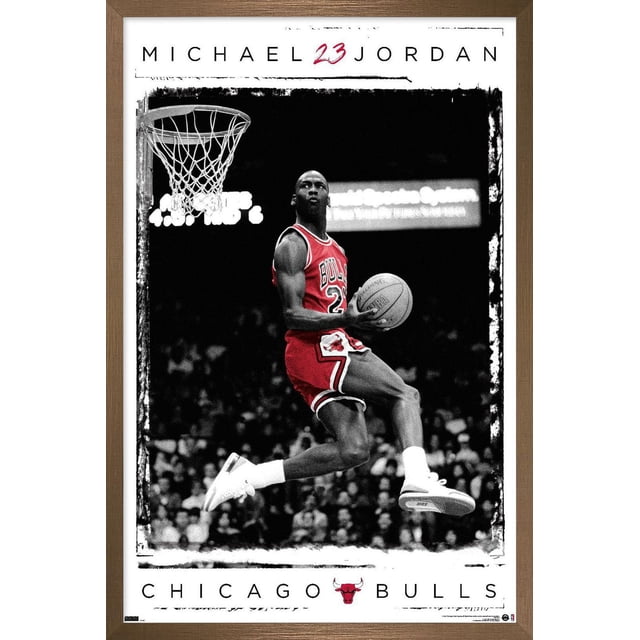 Michael Jordan - Dunk Wall Poster, 14.725" x 22.375" Framed depicting a basketball player in a red Chicago Bulls jersey number 23 mid-air performing a dunk with a basketball, set against a black-and-white crowd background, framed in light brown wood with a premium satin finish.