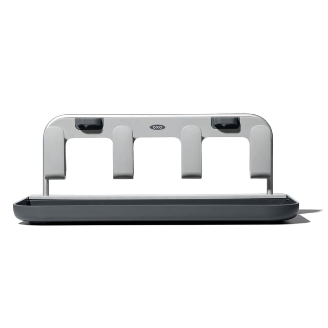 OXO Softworks Bottle Drying Rack in grey with a rectangular base and four vertical supports designed to hold and dry baby bottles, lids, and straws, made from BPA-free material with raised edges to keep lids secure and a disassemblable design for compact storage.