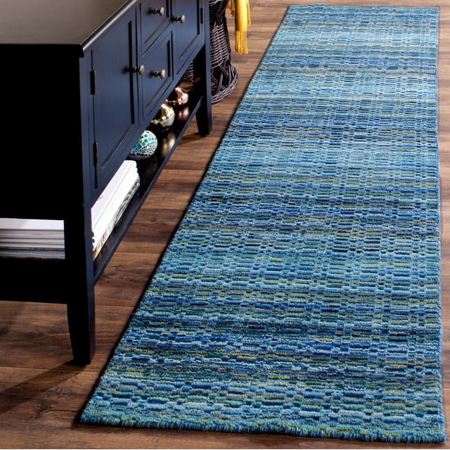 Safavieh Himalaya Branden Overdyed Stripes Area Rug in blue tones with a hand-loomed wool texture and subtle striped pattern, laid on a hardwood floor beside a black cabinet, suitable for use as a runner rug in modern home interiors.