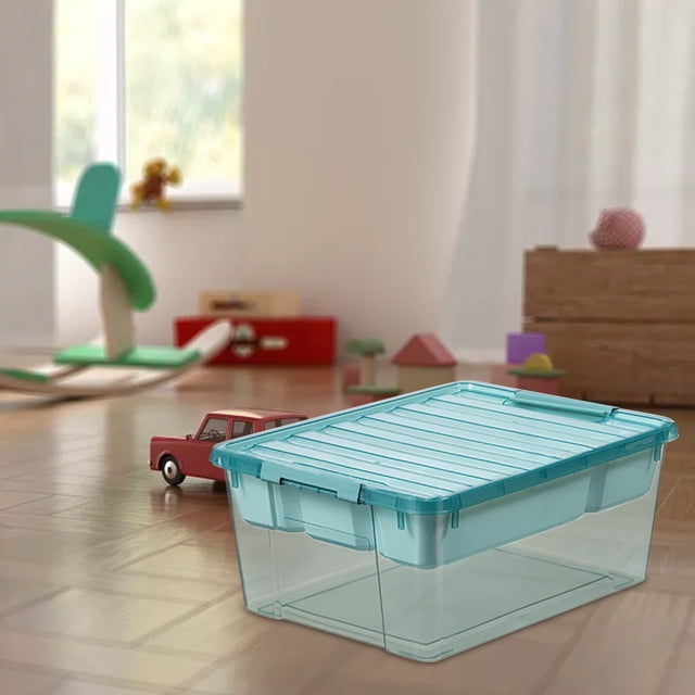 EQWLJWE Toy Storage Containers with Lids, a brick-shaped kids toy organizer box made of clear plastic, shown in a playroom setting. The stackable design features a transparent base and lid for easy visibility of contents. The box includes five removable compartmentalized trays for organizing building blocks, dolls, art supplies, and other small items. The teal lid has a secure clasp to prevent spills and doubles as a base plate compatible with building blocks.