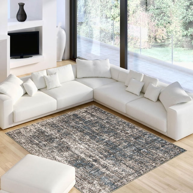 ECARPET Isla Blue, Grey Rug featuring a textured abstract pattern in blue and grey tones, placed on light hardwood flooring in a bright living room with a white L-shaped sectional sofa and ottoman, ideal for accenting contemporary interior spaces.