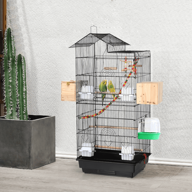 Yaheetech 39'' bird cage in black, designed for mid-sized parrots, cockatiels, or parakeets. The cage features a spacious design with rust-proof painted metal wires, 0.4-inch bar spacing, and a slide-out tray for easy cleaning. Includes accessories such as feeders, wooden perches, toys, a ladder, and a swing. The cage is shown in a home setting with two green birds inside, surrounded by colorful toys and wooden attachments.