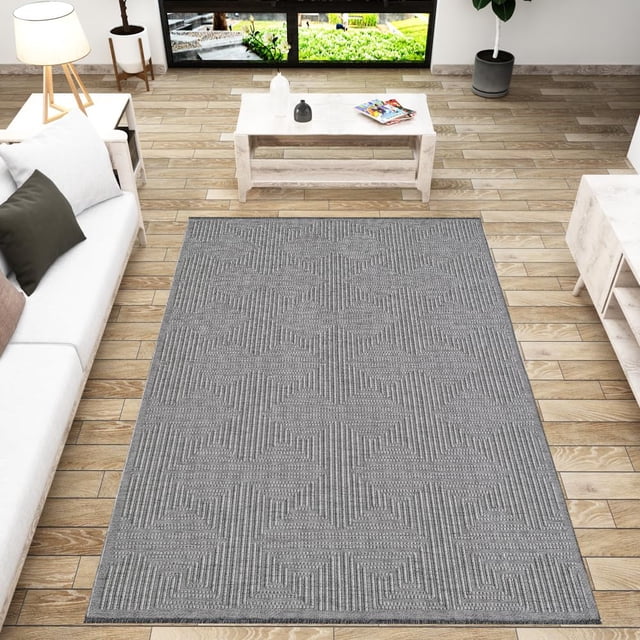 BY COCOON Area Rug 4'x6' in grey displayed in a modern living room with wooden flooring. The rug showcases a subtle geometric pattern and a low pile thickness of 0.2 inches, suitable for high-traffic areas, entryways, and placement under furniture. Made in Turkey with durable cotton and chenille materials, it is resistant to stains, fading, and shedding. This washable runner rug features a non-slip backing for added safety and functionality.