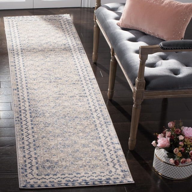 SAFAVIEH Brentwood Dolkar Abstract Geometric Area Rug runner with beige base and blue geometric motifs, made of soft synthetic yarns in close cut pile, placed on dark hardwood floor beside a gray tufted bench with wooden legs and pink cushion, ideal for traditional and transitional decor and suitable as a hallway accent rug.