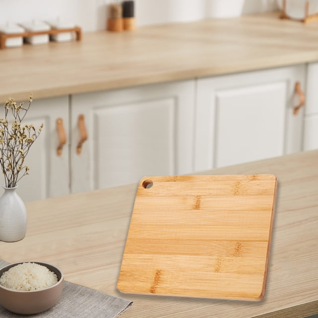 kcavykas Big Deals Items chopping board crafted from natural bamboo wood, featuring a square design with rounded edges and a convenient hanging hole. Measuring 18x18x1cm, this durable kitchen board is ideal for cutting fruits, vegetables, and other food items. Displayed on a light wood kitchen countertop, it complements modern kitchenware.
