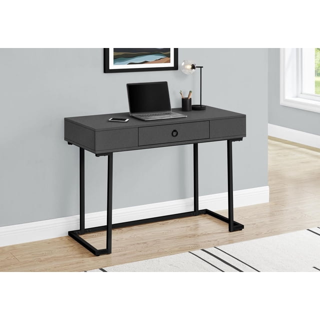Monarch Specialties Computer Desk in grey laminate with black metal reverse C-shaped legs, featuring one large center drawer with a black metal ring pull, sized 42 inches long, shown with a laptop, smartphone, pencil holder, and desk lamp in a modern home office space, also suitable as a console table or accent piece.