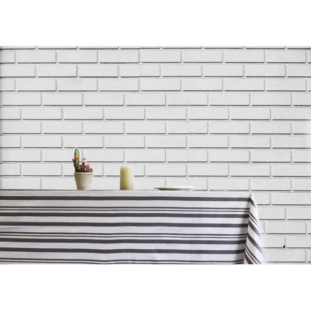 Fabstyles Broadway 100% Cotton Stripe Table Cloth in grey with horizontal stripes on a rectangular table, styled with a small potted cactus, beige candle, and white plate against a white brick wall, suitable for indoor dining and protecting table surfaces.