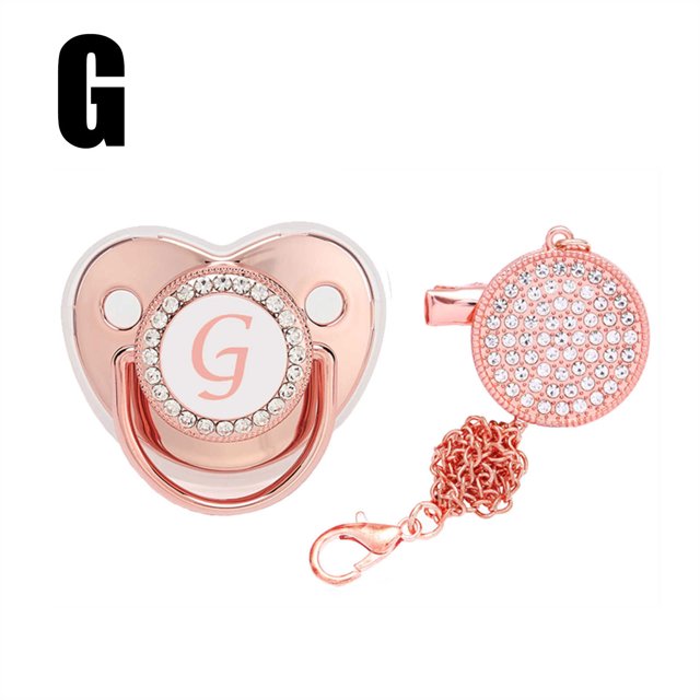 DPTALR Baby Pacifier 26 Letter Name Initial Clip Silicone Infant Nipple Bling Newborn Pacifier in rose gold with rhinestone embellishments. The pacifier features a customizable initial 'G' on the front and includes a matching anti-lost clip with a chain. Made of food-grade silicone, it is safe for babies and designed to support oral development. The clip can be attached to clothing or strollers to prevent loss. Ideal as a baby gift for special occasions.