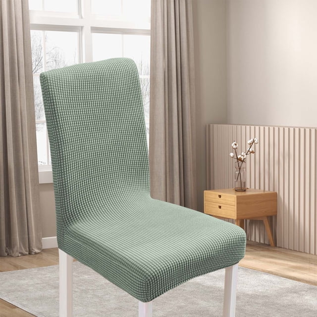 Under 10 dining room chair cover in a colorful design, made of elastic polyester material, shown on a dining chair in a modern room setting. The washable chair protector features a textured pattern and strapless design with an elastic bottom to prevent slippage. Suitable for kitchen chairs and ideal for protecting chairs from stains, wear, and scratches.