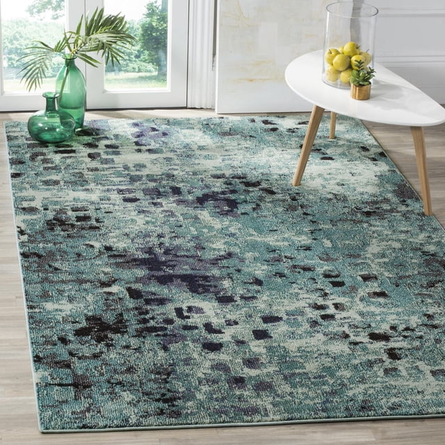 Safavieh Monaco Driskoll Abstract Area Rug featuring a blue and teal erased-weave abstract pattern with black accents, power-loomed polypropylene texture, placed on light wood flooring in a bright room with a white modern table holding a glass vase of lemons and a small plant, and green glass vases with palm leaves near a window, ideal for adding Bohemian-chic flair to home decor.