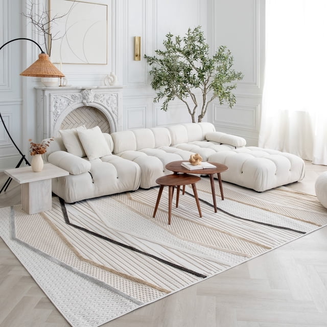 Rug Branch Maison Indoor Area Rug featuring beige and cream geometric textured stripes in taupe and charcoal, placed in a bright living room under a tufted white sectional sofa and round wooden nesting tables. Ideal for high-traffic areas like kitchens and hallways, the room includes a white ornate fireplace, a large green potted plant, and sheer white curtains.