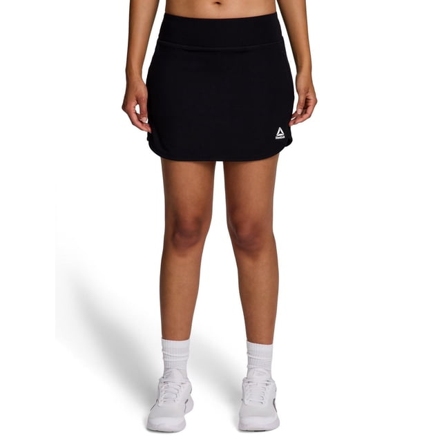 Reebok Jupe-short de Fairway pour Femme Noire à Coupe Ajustée, Taille Élastique, Petit logo Reebok Blanc à l'Avant, Ourlet Gauche, Tissu Qui Évacue l'Humidité et Poche Latérale Zippée, Montré de l'Avant sur Fond Blanc.