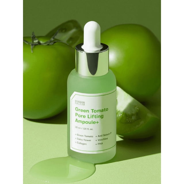 Sungboon Editor Green Tomato Pore Lifting Ampoule+ 30ml frosted glass dropper bottle on a green surface with whole and sliced green tomatoes, showing spilled light green serum, formulated to tighten pores and improve skin elasticity with green tomato extract and anti-sebum complex.