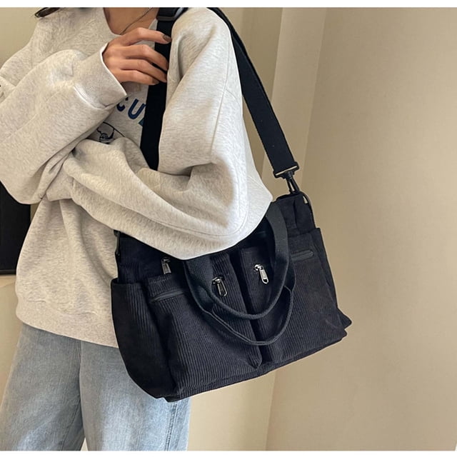Meitianfacai Corduroy Tote Bag For Women 2024 New Japanese And Korean Multi Compartment Commuting Large Capacity Shoulder Crossbody Bag in black. The bag features a soft corduroy material with a solid color design, multiple zippered compartments, and an adjustable shoulder strap. It is shown being carried by a person wearing a grey sweatshirt and jeans, highlighting its versatility for daily use.