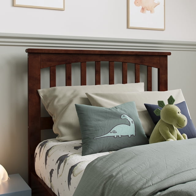 Tête de Lit Simple en Bois Mission en Noyer Présentant un design Mission Classique avec Lattes Verticales et Moulure en Couronne. Fabriquée en Bois Franc Massif durable, Elle Est Présentée Attachée à un Lit avec une Literie Neutre et des Coussins Décoratifs, Incluant un Coussin à Thème Dinosaure et un Jouet en Peluche. la Finition Noyer Ajoute de la Chaleur à l'Environnement de la Chambre.