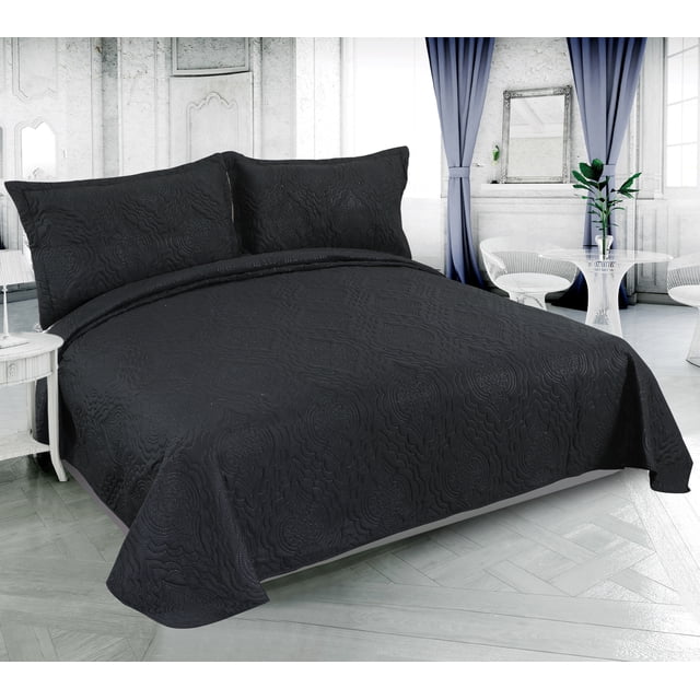 Marina Decoration Solid Embossed Pinsonic Coverlet Bedspread Bedding Ultra Soft Summer Quilt Set with Shams in black, displayed on a bed in a bright room with white walls and blue curtains. The quilt and pillow shams feature a solid black color with an embossed pinsonic pattern, made from 100% brushed microfiber with polyester fill. This lightweight, breathable, reversible quilt set is suitable for all-season use and can also be used as a bedsheet or blanket. The room includes a white side table and a glass table with white chairs, highlighting the quilt's modern, elegant design.