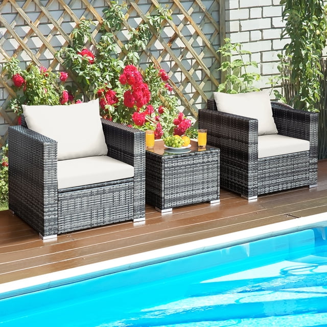 Gymax 3PCS Rattan Patio Conversation Furniture Set with two mix grey rattan single sofas featuring white cushions and a coffee table with a tempered glass top. The set is arranged outdoors near a pool, accented by red flowers and lush greenery, ideal for patios or backyards.