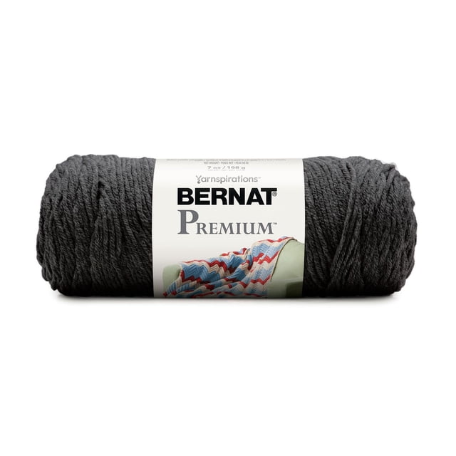 Bernat® Premium TM Fil, Acrylique #4 Moyen Worsted, 7oz/198g, 360 Yards en Gris Foncé, un Écheveau Bien Enroulé avec une Étiquette Blanche Présentant le logo Bernat Premium et un afghan Tricoté Multicolore sur une Chaise Verte, Lavable à la machine et Convient aux Projets de Tricot et de crochet.